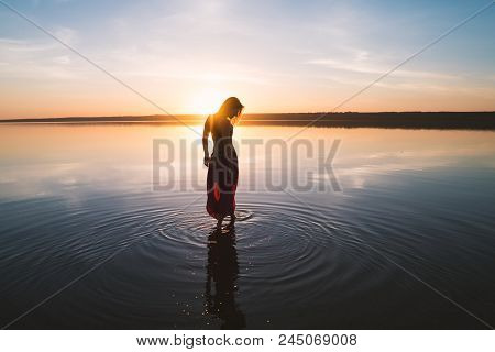 Silhouette Woman On The Beach At Sunset . She Stands In Water. Morning Natural Stretch Warm-up Train