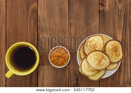 Pancakes, Fritters With Apricot Jam And Tea In Yelow Cup On The Wooden Table. White And Gray Brick B