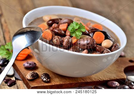 Close-up Of Bowl Of Bean Soup With Large Beans , Spoon, Carrots, Parsley And Marjoram