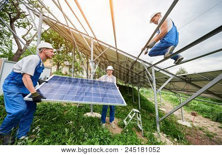 Installing Of Stand-alone Solar Photo Voltaic Panel System. Three Technicians Lifting Big Solar Modu