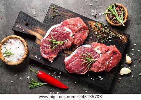 Fresh Meat. Raw Beef Steak On A Cutting Board With Rosemary And Spices On Dark Stone Table. Top View