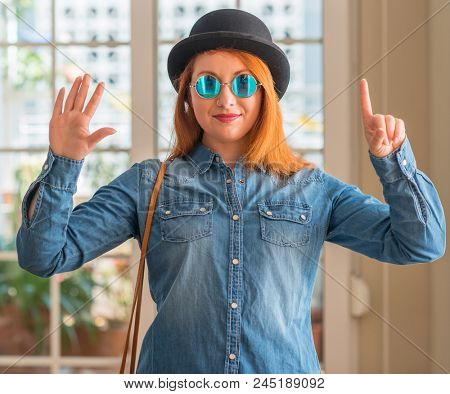 Stylish redhead woman wearing bowler hat and sunglasses showing and pointing up with fingers number six while smiling confident and happy.