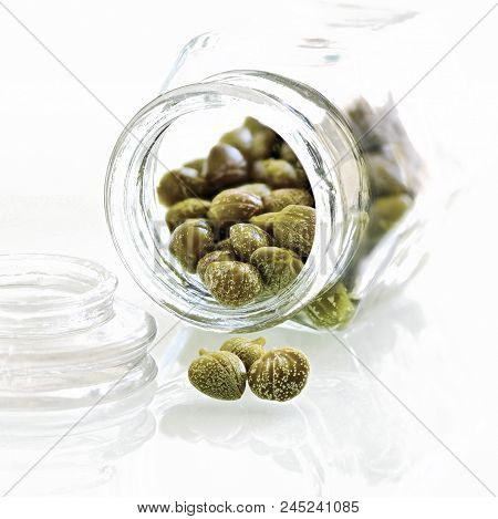 Organic Capers, Capparis Spinosa In A Glass Jar Macro Shot In A Square Format Light Background To Ad