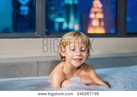 Happy Little Baby Boy Sitting In Bath Tub In The Evening Before Going To Sleep On The Background Of 