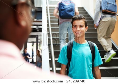Male High School Student Talking With Teacher In Busy Corridor