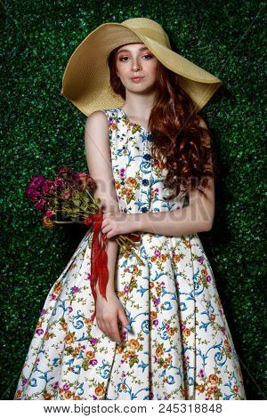 Portrait of a cute girl teenager wearing summer dress and hat over lawny background. Beauty, fashion.