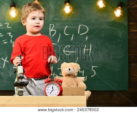 Kid Boy Near Microscope In Classroom, Chalkboard On Background. First Former Interested In Studying,