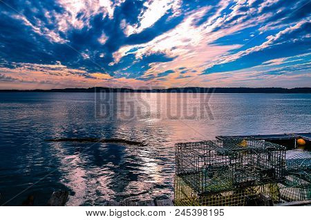 The setting sun over the Johnson Bay in Lubec, Maine with a colorful cloudy sky in the background and lobster traps in the foreground