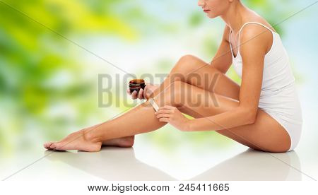 beauty, depilation, epilation, hair removal and people concept - beautiful woman with applicator applying depilatory wax to her leg over green natural background