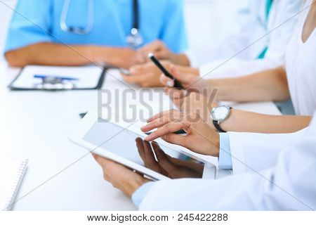 Doctor Using Tablet Computer At Medical Meeting, Closeup. Group Of Colleagues At The Background.