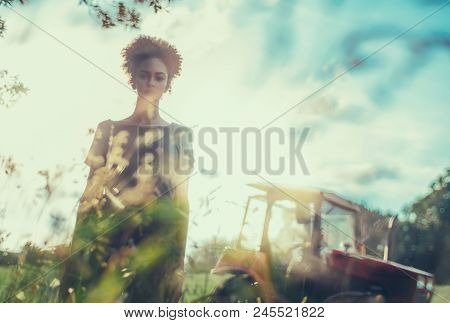 Creative Shot Of A Young Serious Black Girl With Curly Afro Hair Standing On The Field With Tractor 