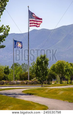 American Flag And The Utah Flag On A Roundabout In Eagle Mountain, Utah. Winding Sidewalk In Foregro