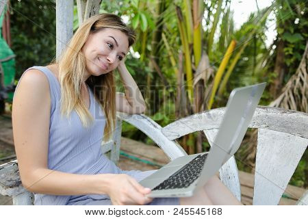 Happy Woman Using Laptop And Sitting In Exotic Garedn With Palms In Background. Concept Of Summer Va