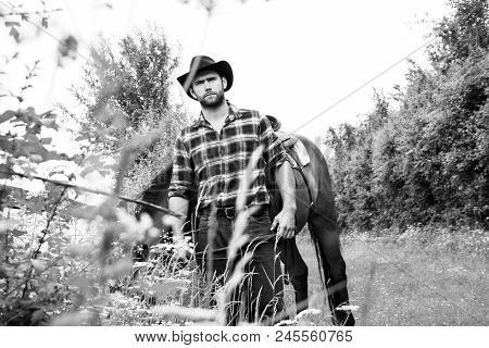 Good Looking, Hunky Cowboy With Boots, Chequered Shirt And Hat Stands In Front Of His Stallion, Hors