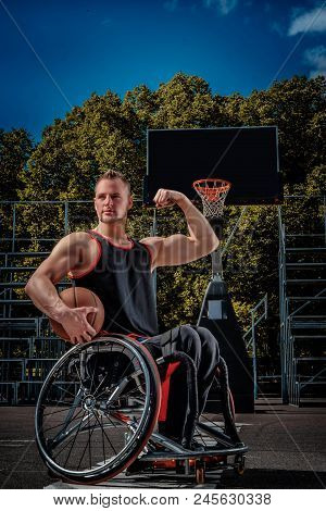 Strong Basketball Player In A Wheelchair Pose With A Ball On Open Gaming Ground.