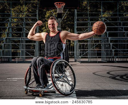 Happy Basketball Player In A Wheelchair Pose With A Ball On Open Gaming Ground.