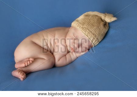 Newborn Baby Lying Ina Beige Cap On A Blue Background. Imitation Of A Baby In The Womb. Beautiful Li