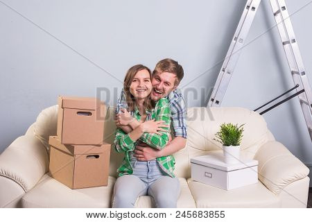 Happy Young Couple Sitting On The Floor In New Apartment After Moving In And Looking At Camera