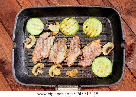 Top View Of Grill Pan With Grilled Slices Of The Streaky Bacon, Vegetable Marrows And Mushrooms On A