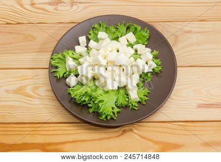 Brown Dish With Mozzarella Cheese Sliced Into Small Cubes On Lettuce Leaves On Wooden Surface