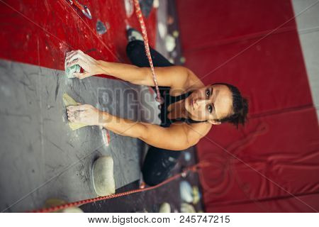 High Angle View Of Professional Sport Female Rock Climber On Red Vertical Wall Preparing To Competit