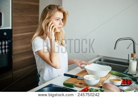 Smiling Caucasian Woman Making Healthy Meal And Reading Message At Phone In The Domestic Kitchen.