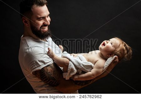 Portrait Of Handsome Strong Beared Man Holding On Hands Adorable Little Baby Over Black Background W
