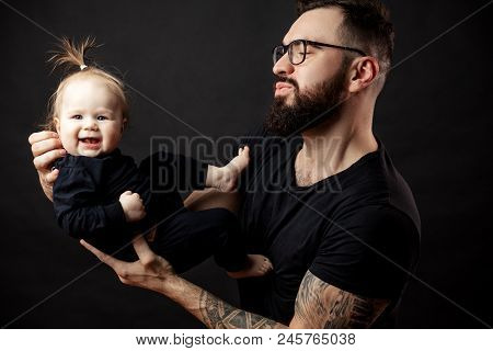 Happy Handsome Father In Perfect Fit, Looking At His Infant Baby Girl In His Hands, Fondling And Nur