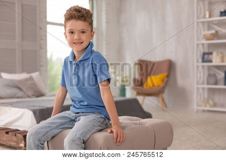 Cute Boy. Little Pleasant Looking Cute Boy Wearing Dark Blue Shirt And Denim Jeans Sitting On Hassoc