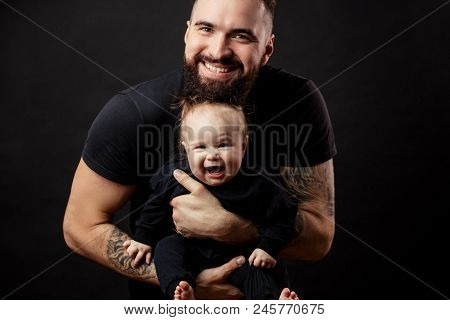 Amasing Portrait Of Handsome Young Man With Strong Tattooed Arms Embracing His Little Adorable Joyfu