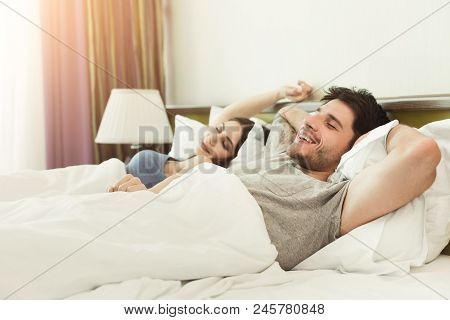 Happy Young Couple Waking Up Snd Lying With Closed Eyes In The Morning On Bed