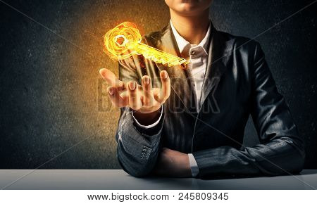 Closeup Of Businessman In Black Suit Keeping Flaming Key Symbol In Hand With Dark Wall On Background