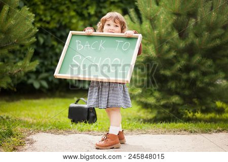 Cute Caucasian Little Girl Holding Chalkboard Written Back To School. With A Smile. Ready And Happy 