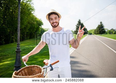 Portrait Of Cheerful Positive Attractive Man In White Outfit Having Bike Gesturing Two Fingers V-sig