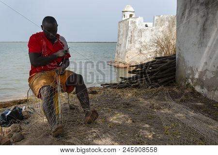 Cacheu, Republic Of Guinea-bissau - February 1, 2018: Fishermen Repairing Fishing Nets Next To The C