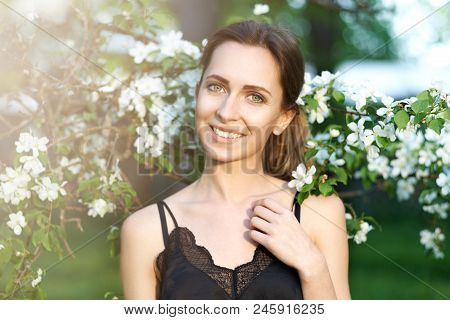 Young Beautiful Woman Enjoying Of Blooming Tree On A Sunny Day. Portrait Of Young Woman Smiling In T