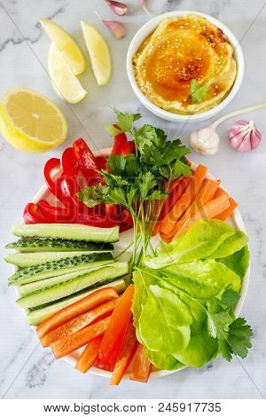 Hummus, Different Vegetables And Lettuce Leaves With Lemon And Garlic On A Light Background. Vegan F