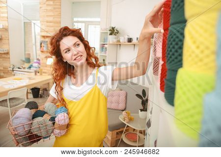 Taking Thread. Red-haired Beaming Craftswoman Lifting Her Left Hand For Taking Bright Red Crochet Th