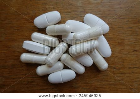 Handful Of White Caplets Of Calcium Citrate And Capsules Of Magnesium Citrate On Wood