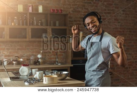 Happy Black Man In Earphones Listening To Music And Dancing While Baking In Kitchen