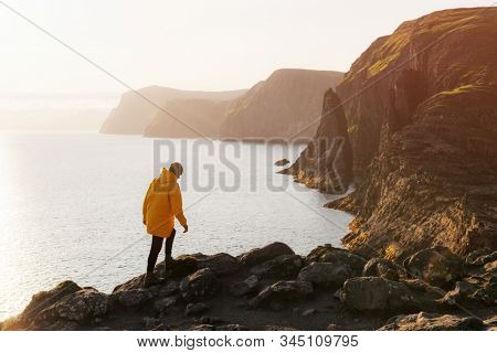 Tourist in yellow jacket looks at cliffs near Sorvagsvatn lake on Vagar island, Faroe Islands, Denmark. Landscape photography