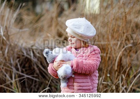 Outdoor Portrait Of Little Cute Toddler Girl In Pink Coat And White Fashion Hat Barret Playing With 