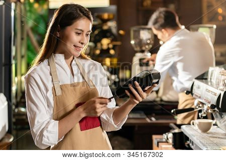 Asian Barista make payment with customer credit card using  EMV chip technology for coffee purchase at a cafe bar.