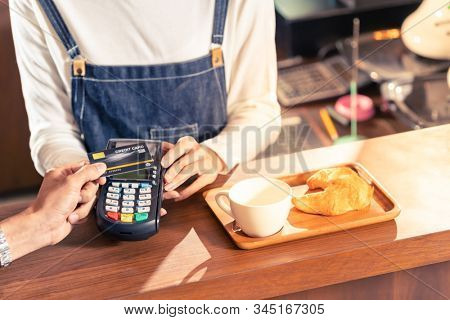 Close-up of asian customer using his credit card with contactless nfs technology to pay a barista for his coffee purchase at a cafe bar.