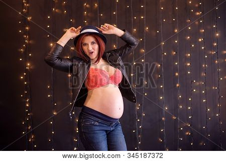 Audacious Young Pregnant Woman At Second Trimester In Orange Bra, Jacket, High Waist Jeans And Hat P
