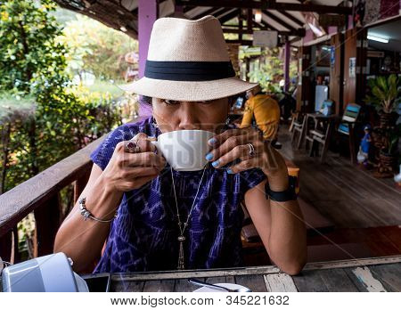 Thai Woman With Fedora Hat Sitting At Cafe Drinking Coffee In Pak Nam Pran Thailand