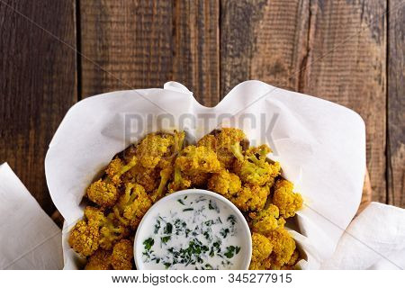 Top View Crispy Cauliflower With Sauce On White Parchment Paper On Wooden Background