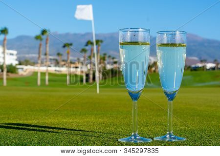 Two Glasses With  Bubbles White Champagne Or Cava Wine Served On Green Golf Club Grass With Mountain