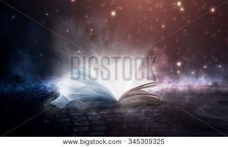 Open Book Magic. Dark Background Magic. An Open Book On A Wooden Table Under The Night Sky Against A