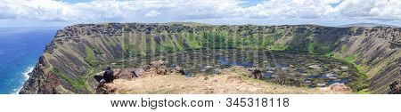A Man Sits On The Edge Of The Rano Kau Crater On Easter Island, Chile Overlooking The Pacific Ocean;